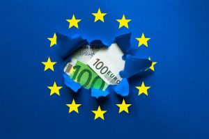 Europa-Flagge mit Loch, darin Euro-Scheine (Foto: Freepik, mikeygl) - Eurozone Inflation aktuell: Teuerung im März 2024 und EZB-Zins-Prognose