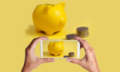 Hände nehmen Bild mit Smartphone Sparschwein und Geld auf