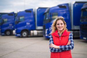 Junge Lkw-Fahrerin, im Hintergrund blaue Lastkraftwagen (Foto: freepik, aleksandarlittlewolf) - Erster deutscher Logistiker führt die 4-Tage-Woche ein