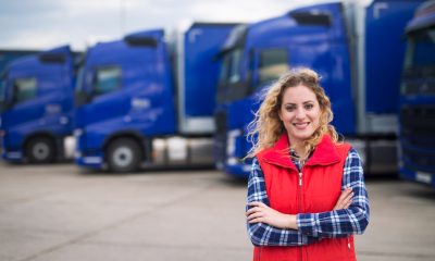 Junge Lkw-Fahrerin, im Hintergrund blaue Lastkraftwagen (Foto: freepik, aleksandarlittlewolf)
