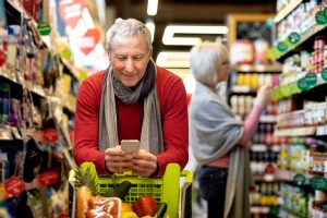 Älterer Mann im Supermarkt schaut auf sein Handy (Foto: Freepik, prostock-studio) - Boomer Generation: Surfen, Shoppen, Finanzen – so ticken Menschen zwischen 55 bis 75