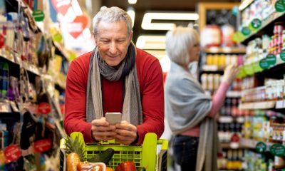 Älterer Mann im Supermarkt schaut auf sein Handy - Boomer Generation: Surfen, Shoppen, Zahlen (Foto: Freepik, prostock-studio)