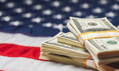 US-Dollar-Noten vor einer Flagge der USA - Leitzins Fed Entscheid USA Inflationsdaten (Foto: Freepik, BillionPhotos)