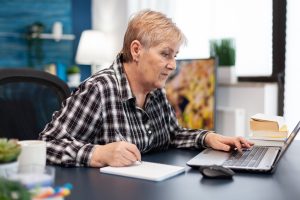 Ältere Frau arbeitet am Schreibtisch mit Laptop - Anlage in Aktien für die Altersvorsorge lohnt sich