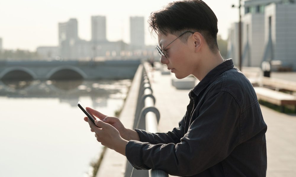 Chinese mit Smartphone an Flussufer (Foto: freepik, pressmaster)