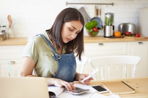 Frau rechnet am Küchentisch mit Taschenrechner (Foto: freepik, shurkin_son) - Haushaltsbuch führen: wirksam Ausgaben senken und Geld sparen – so funktioniert es