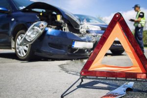 Großes Warndreieck, im Hintergrund ein Unfallsauto (Foto: freepik, aleksandarmalivuk) - Autounfall: Versicherung einschalten – oder als Selbstzahler viel Geld sparen?