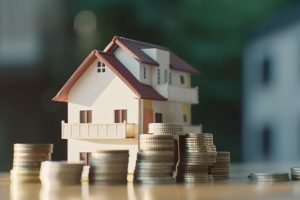 Modell eines Hauses und Geldmünzen (Foto: freepik, mygrafics) - Baufinanzierung: Kreditflaute hält an – Gewerbedarlehen etwas stärker