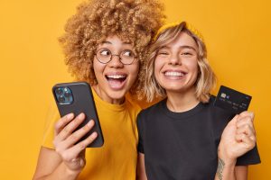 2 junge Frauen mit Smartphone und Kreditkarte (Foto: Freepik, wayhomestudio) - Geld sparen beim Online-Einkauf – 8 Tipps für die heiße Shopping-Zeit