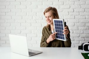 Frau an einem Schreibtisch mit einem Solarmodul in der Hand (Foto: freepik, freepik) - Photovoltaik: Mini-Solaranlagen für Balkon oder Terrasse – so geht's