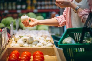 Hand hält Zwiebel an Auslage im Supermarkt (Foto: freepik, senivpetro) - Deutschland: Inflation 10 Prozent - Reallöhne brechen 2022 ein
