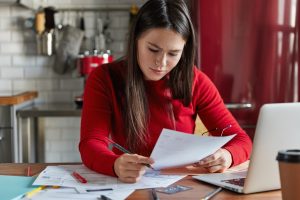 Frau am Küchenstisch liest steuerliche Dokumente (Foto: freepik, wayhomestudio) - Steuer 2023 – neue Entlastungen und Freibeträge