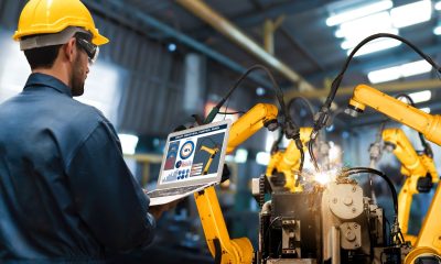 Arbeiter im Blaumann bedient in einer Fabrikhalle Industrieroboter mit einem laptop (Foto: freepik, biancoblue)