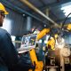 Arbeiter im Blaumann bedient in einer Fabrikhalle Industrieroboter mit einem laptop (Foto: freepik, biancoblue)