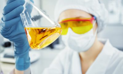 Junge Frau im Chemie-Labor, die ein Teströhrchen mit gelber Flüssigkeit hält