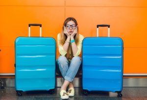 Junge Frau sitzt frustriert zwischen 2 großen Koffern (Foto: freepik, lookstudio) - Fluggastrechte: Klimakleber legen Flughafen lahm – das steht Passagieren zu