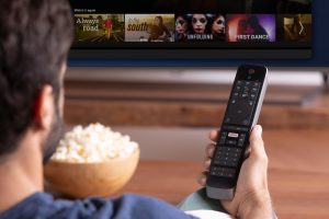 Mann schaut Serien auf Fernseher - Netflix kostet weniger mit Werbung - Netflix Quartalszahlen: Abos Markt Aktienkurs – Prognose und Überblick