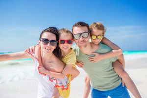 Mann, Frau und 2 Kinder mit Sonnenbrillen im Urlaub am Strand (Foto: freepik, travnikovstudio) - Urlaub 2023: Inflation treibt Hotelpreise – welche Länder sind preiswert?
