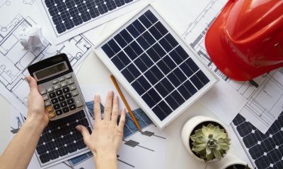 Schreibtisch mit Bauplänen, Solarmodulen, Hände mit Taschenrechner (Foto: freepik)