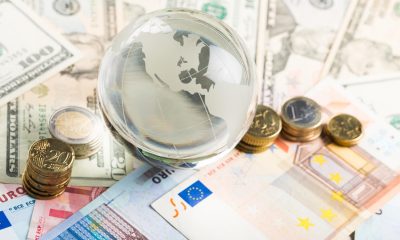 Gläserne Weltkugel auf Euro- und Dollar-Geldscheinen, daneben Euro-Münzen (Foto: freepik, BillionPhotos)